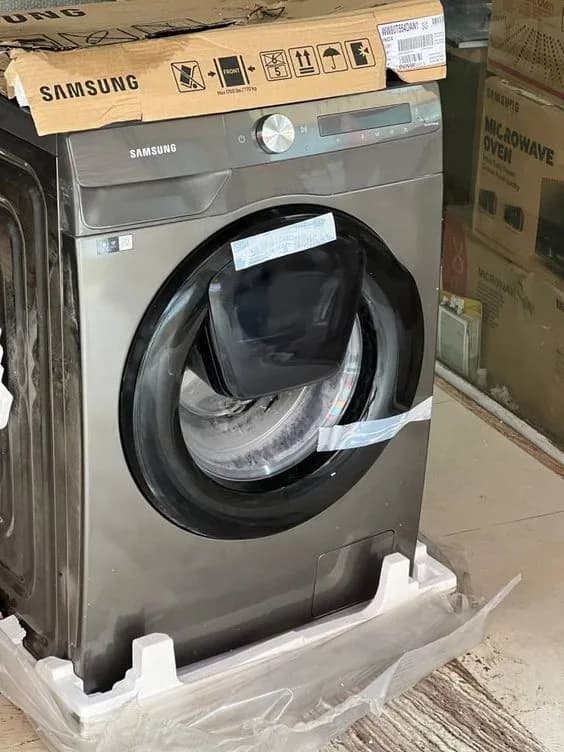A Samsung front-loading washing machine packaged in a warehouse